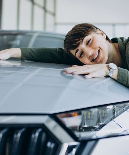 Eine Frau, die sich über ihr neues Auto freut und mit den Händen und der Wange auf der Motorhaube des Autos liegt